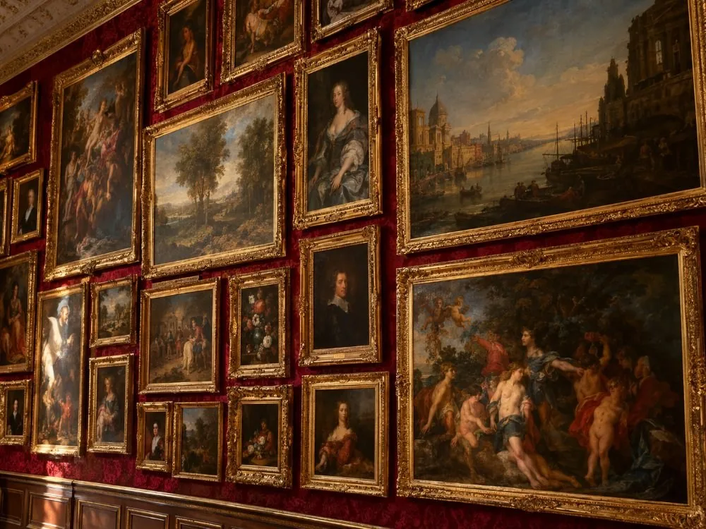 A gallery wing hung salon-style, paintings stacked frame to frame from the dado to the cornice with almost nothing written beside them.